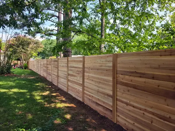 Horizontal cedar board fence running along a yard under trees